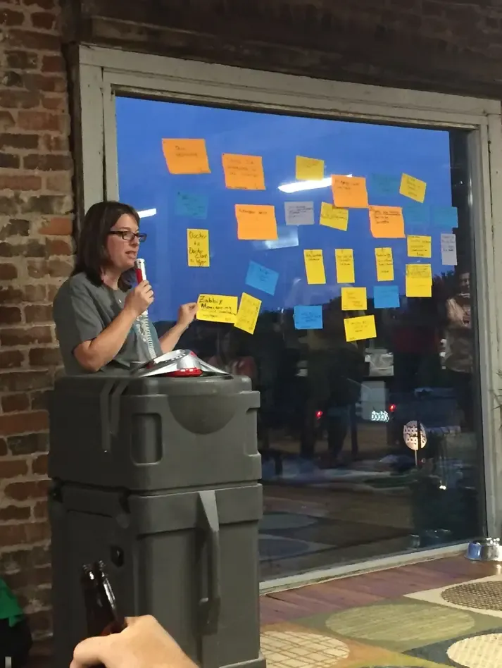 A presenter walks through the sticky-note pitch board at beCamp