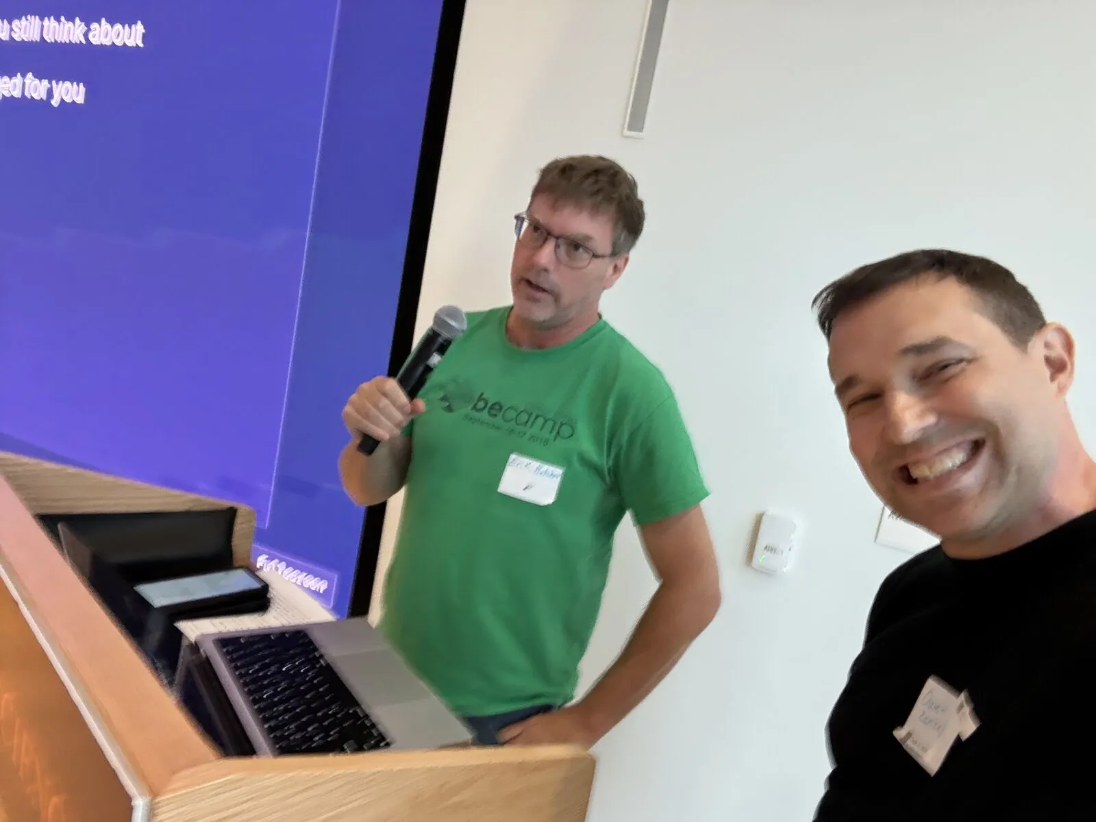 An organizer's selfie with a pitcher in a green beCamp T-shirt speaking at the lectern