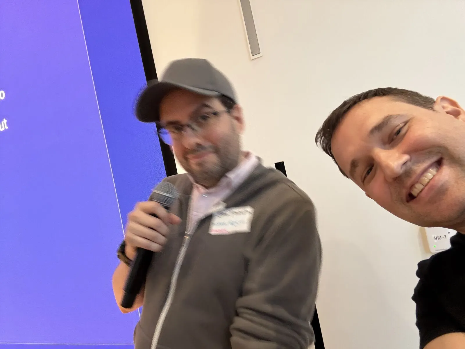 An organizer's selfie with a pitcher in a cap and grey hoodie holding the microphone