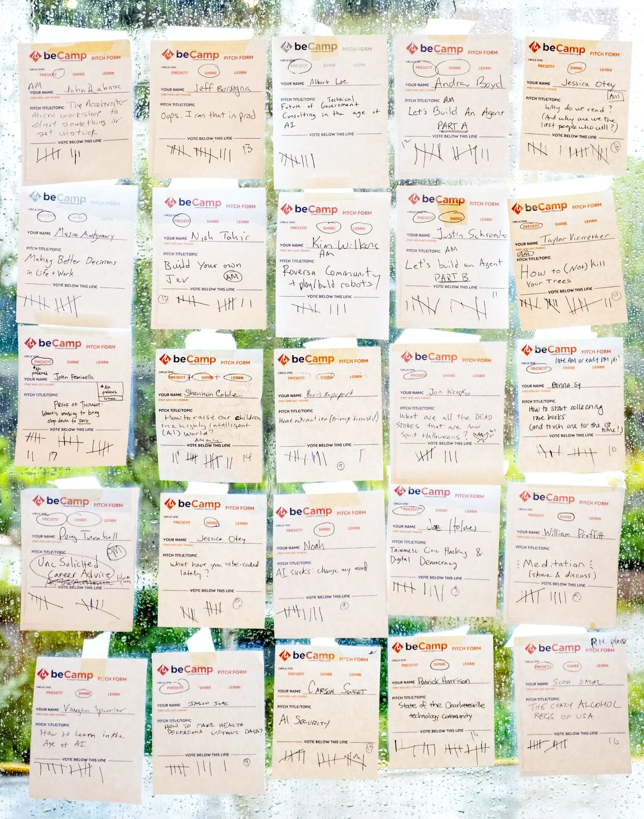 The pitch board: rows of handwritten beCamp pitch cards taped to a window, each marked with vote tallies