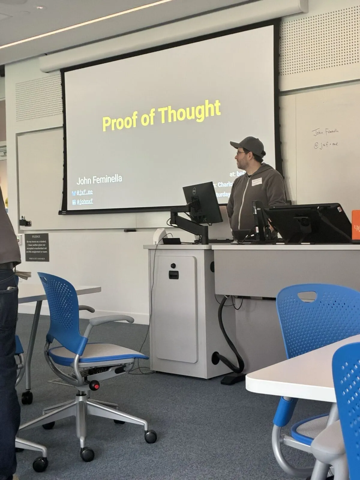 A presenter at the lectern beside the title slide "Proof of Thought"