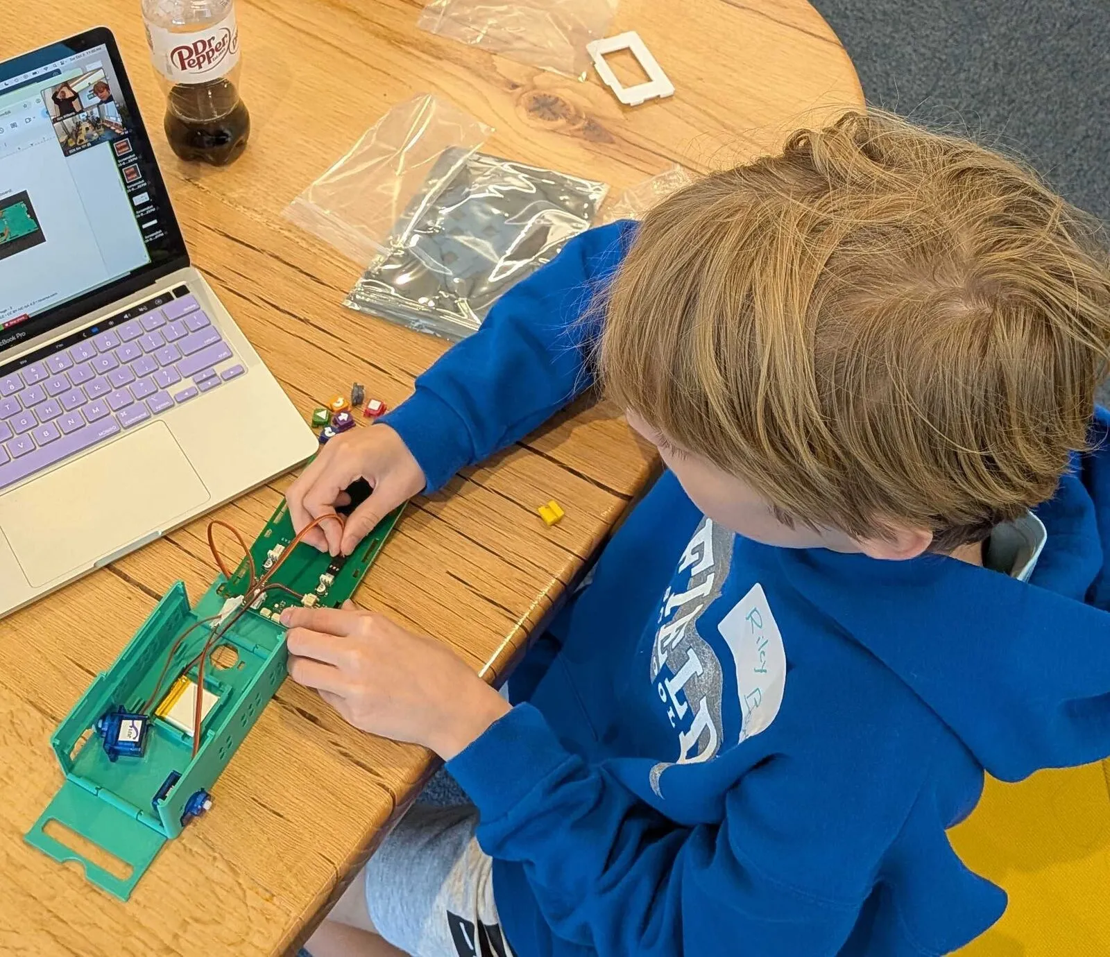 A young attendee wiring electronics into a green robot chassis beside a laptop