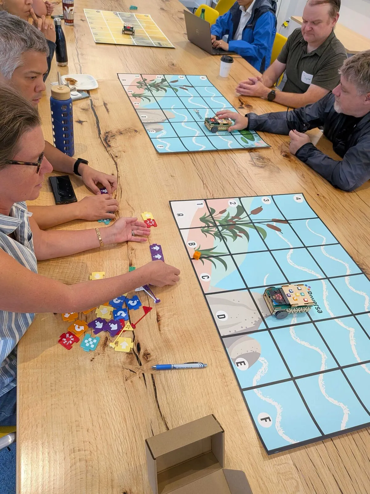 Attendees at a long table playing a robot board game on illustrated grid mats