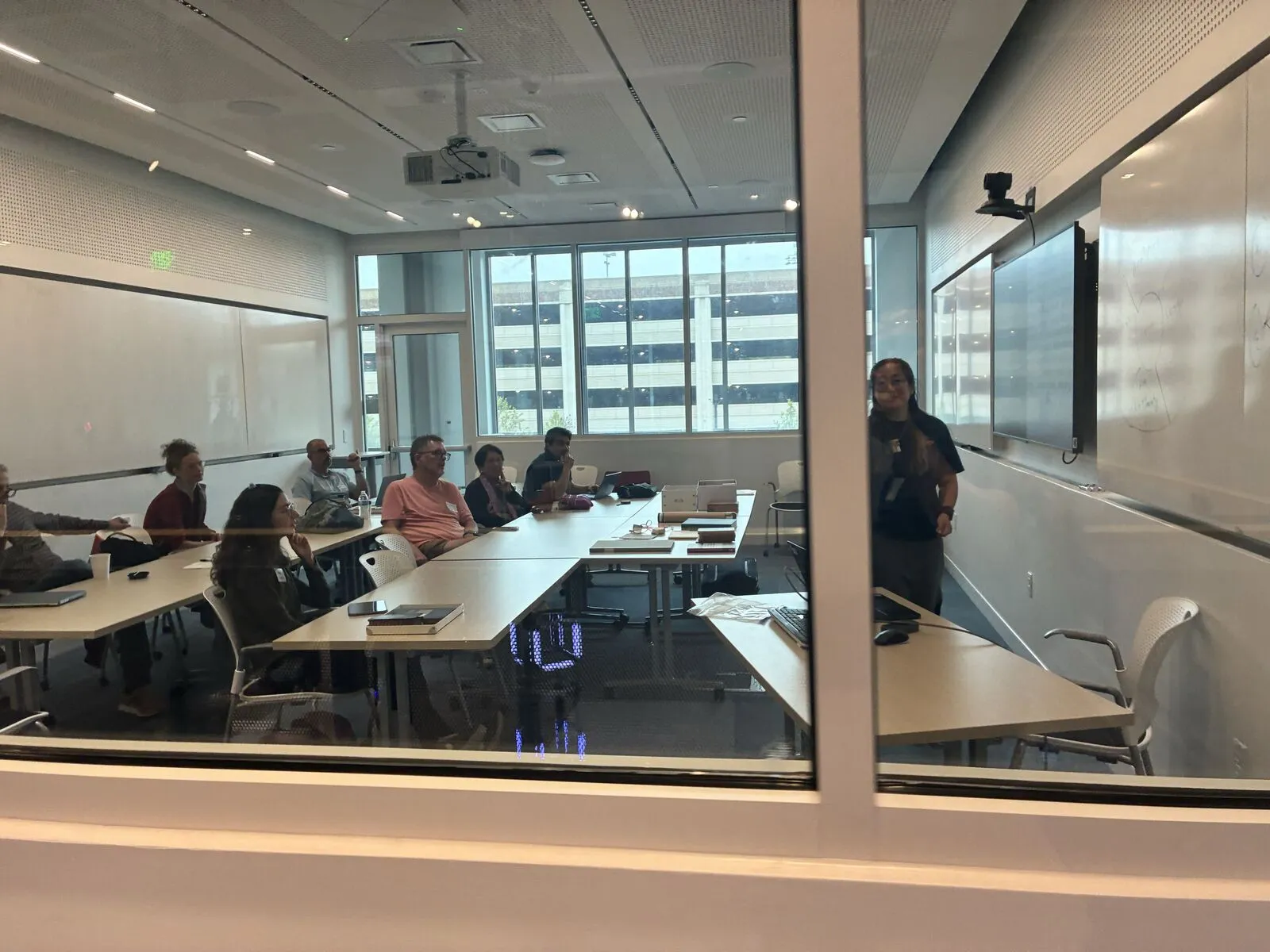 A small session around a long table, seen through a glass wall