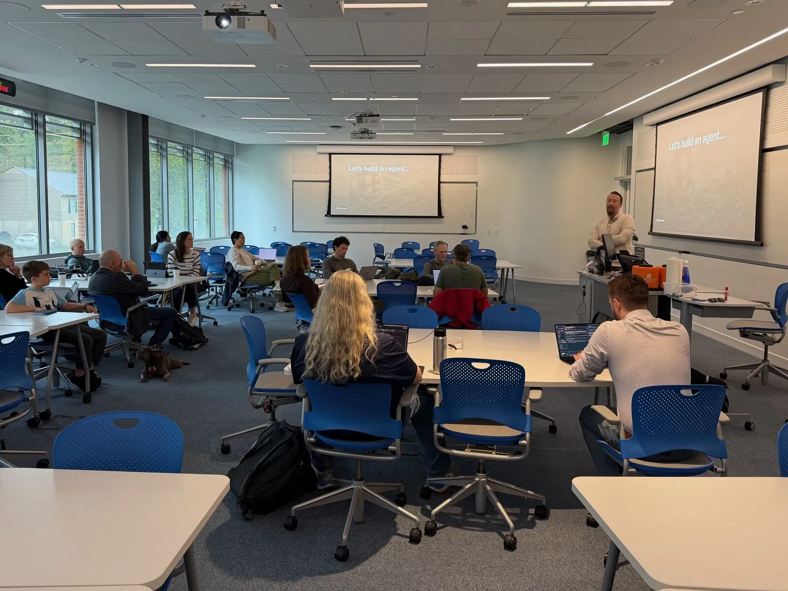 A wide lecture room with attendees at scattered tables during a session